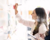 Zwei Frauen arbeiten gemeinsam an einer Wand mit Haftnotizen. Eine Frau schreibt mit einem Stift auf eine Haftnotiz, während die andere sie beobachtet und Notizen macht.