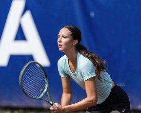 Eine Tennisspielerin bereitet sich auf einen Aufschlag vor, hält einen Schläger in der Hand und schaut konzentriert auf das Spielfeld.