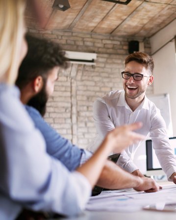 Eine Gruppe von fünf Personen in einem Besprechungsraum diskutiert und arbeitet an Dokumenten. Ein Mann präsentiert aktiv, während die anderen aufmerksam zuhören und Notizen machen.