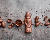 Ein Schokoladenfigur eines Weihnachtsmanns umgeben von Schokoladeneiern und einer kleinen Schüssel mit Schokolade auf einem grauen Untergrund.