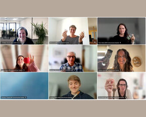 Neun Personen in einem virtuellen Meeting, die verschiedene Gegenstände in die Kamera halten, darunter eine Apfel und Flaschen.