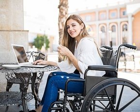 Frau im Rollstuhl mit Notebook an Tisch draußen