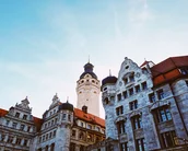 Historische Gebäude mit aufwendiger Architektur und einem hohen Turm im Hintergrund, unter einem klaren Himmel.