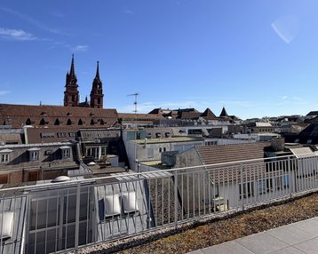 Blick auf die Dächer einer Stadt mit zwei markanten Türmen im Hintergrund und klar blauem Himmel.