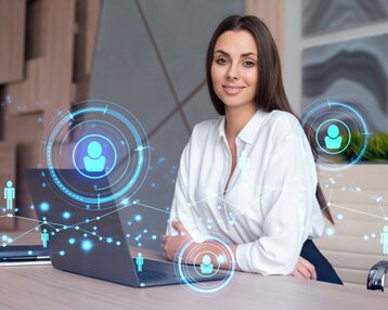 Eine Frau sitzt an einem Schreibtisch mit einem Laptop, umgeben von digitalen Symbolen, die Vernetzung und Kommunikation darstellen.