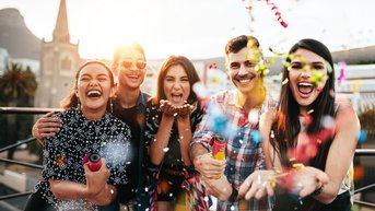 Fünf Personen stehen zusammen und feiern, während sie Konfetti in die Luft werfen. Die Gruppe lächelt und posiert fröhlich.