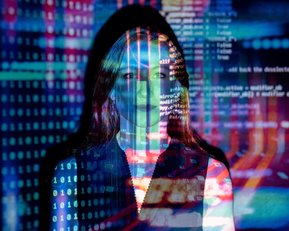 Eine Person steht vor einem Hintergrund aus bunten digitalen Codes und Datenströmen, die über ihr Gesicht projiziert werden. Die Darstellung vermittelt ein Gefühl von Technologie und Datenanalyse.