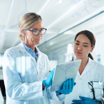 Zwei Wissenschaftlerinnen in Laborkitteln betrachten gemeinsam ein Tablet in einem modernen Labor.