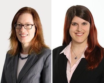 Zwei Frauen in formeller Kleidung, eine mit brünettem, lockigem Haar und Brille, die andere mit langen, glatten, rotbraunen Haaren. Beide lächeln freundlich in die Kamera.
