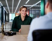 Eine Frau in einem grünen Hemd sitzt an einem Tisch und spricht mit einem Mann. Auf dem Tisch steht eine Statue der Justitia.