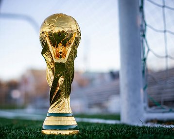 Der FIFA-Weltmeisterschafts-Pokal steht auf dem Rasen vor einem Fußballtor, glänzend und goldfarben.