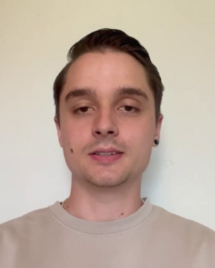 Ein junger Mann mit kurzen, dunklen Haaren trägt ein helles Sweatshirt. Er steht vor einem neutralen Hintergrund und schaut direkt in die Kamera.