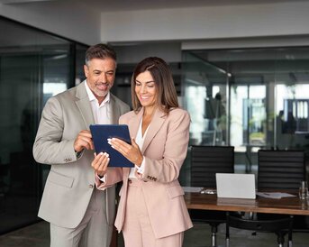 Ein Mann und eine Frau in formeller Kleidung betrachten gemeinsam ein Tablet in einem modernen Büro.