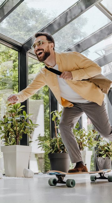 Mann in Anzug fährt auf einem Skateboard in einem modernen Raum mit großen Fenstern und Pflanzen.